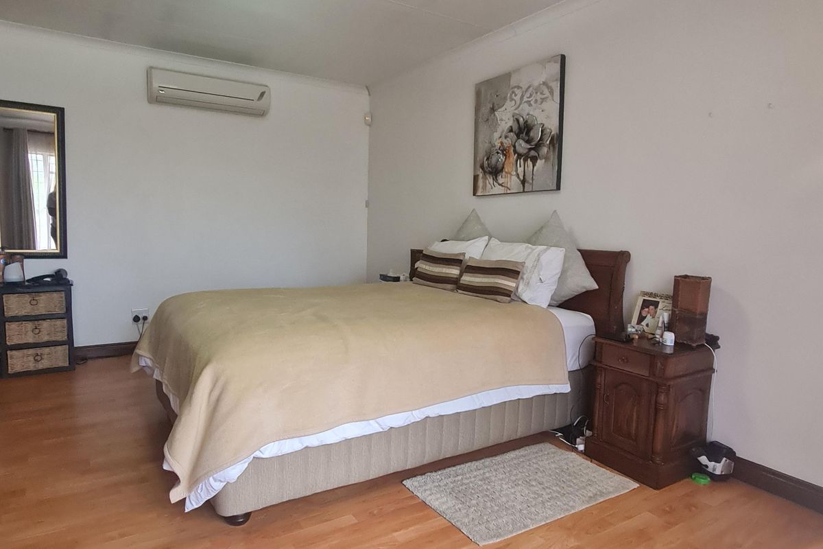 A spacious bedroom featuring laminate flooring, a wall-mounted air conditioning unit, and a central ceiling light fixture.