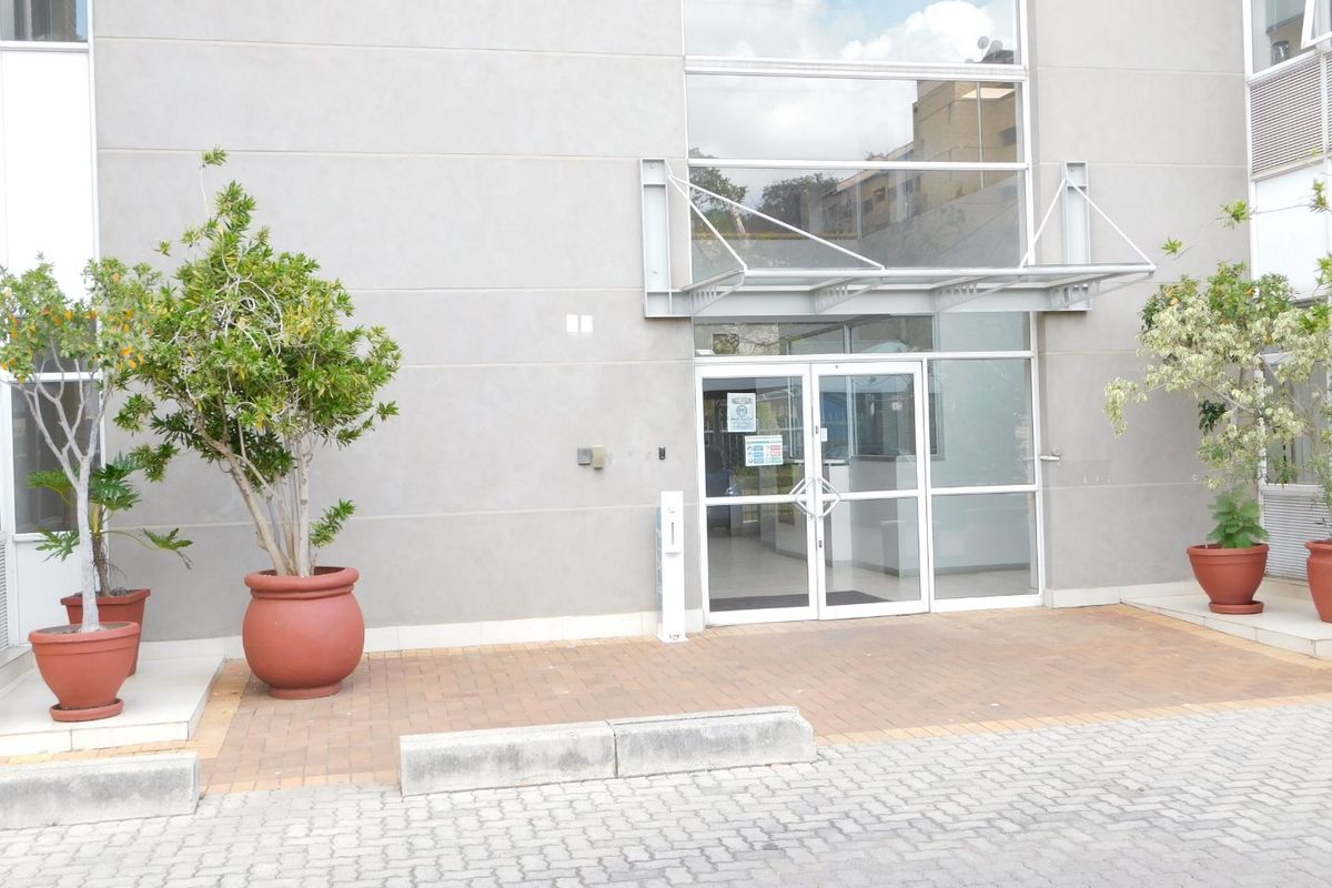 Modern office building entrance featuring a glass facade, metal canopy, and paved pedestrian access area.