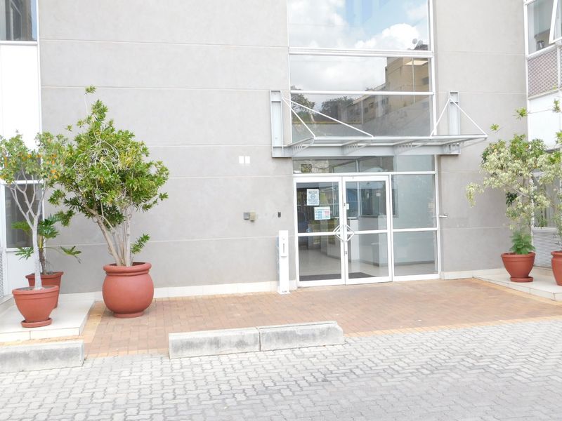 Modern office building entrance featuring a glass facade, metal canopy, and paved pedestrian access area.