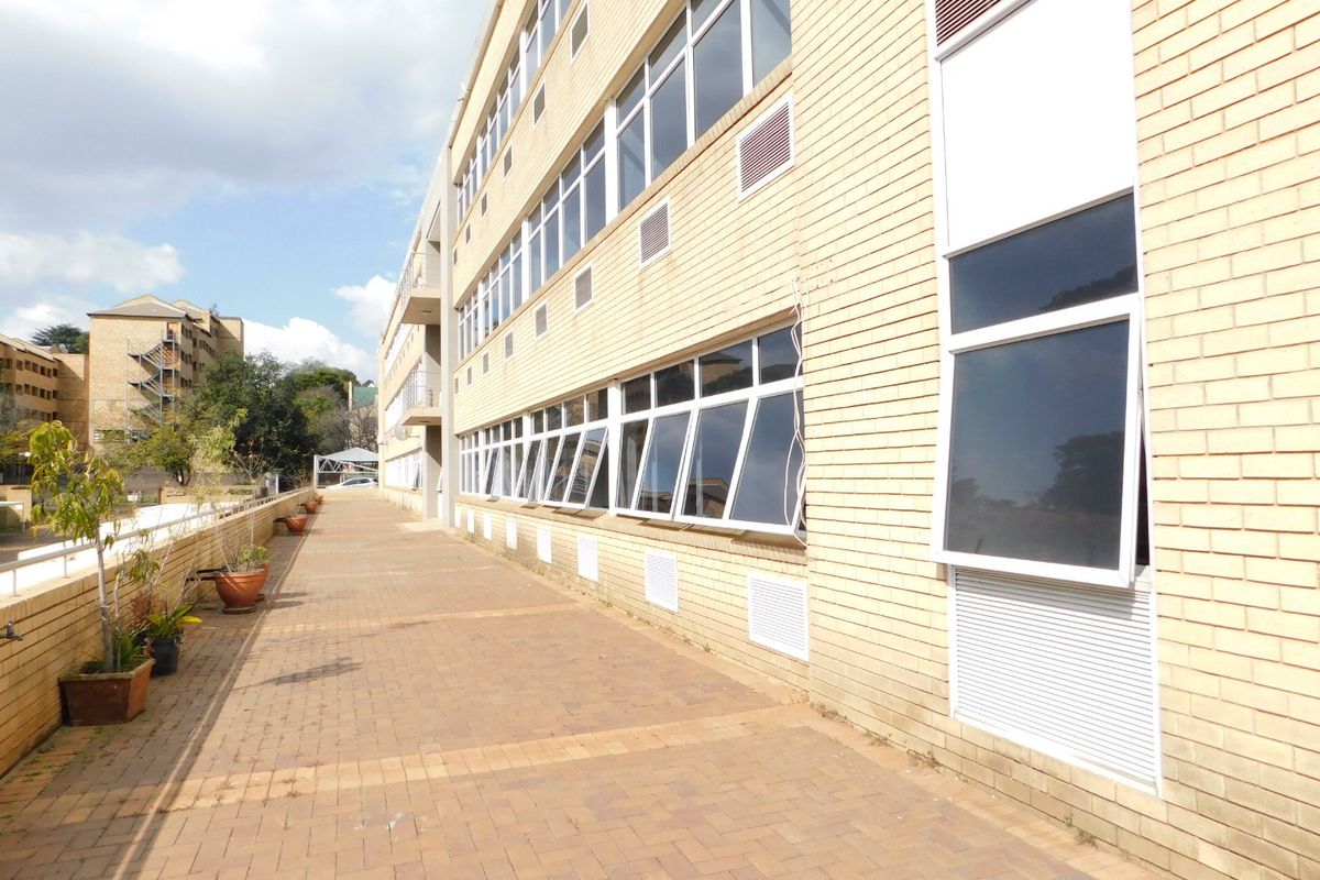 Exterior view of a multi-story office building featuring a brick facade, paved walkway, and rows of aluminium-framed windows.