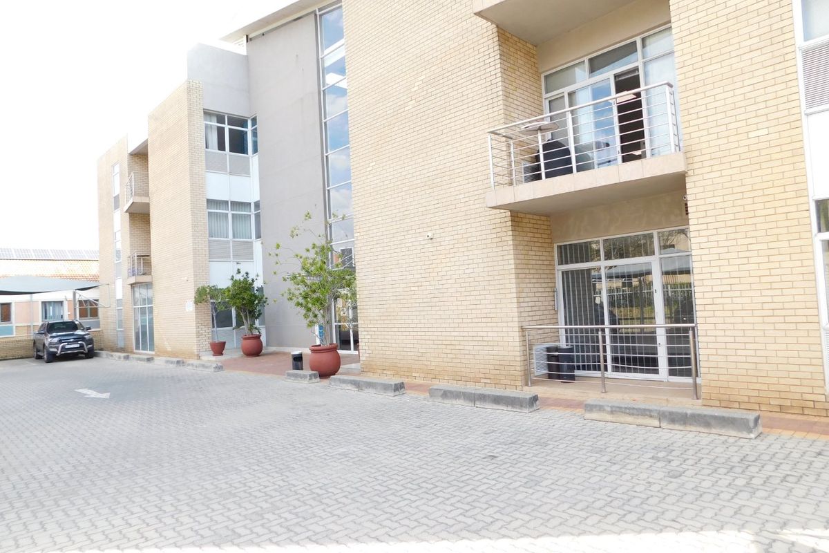A modern multi-story office building featuring a brick facade, paved driveway, and private balconies with metal railings.