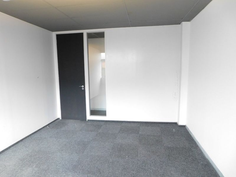 A vacant office space featuring grey carpet tiles, a suspended ceiling, and a modern door with an adjacent glass sidelight.