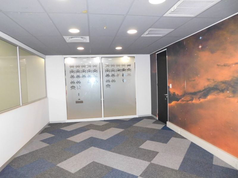 Empty office space featuring patterned carpet tiles, a suspended ceiling with recessed lighting, and a glass partition wall with decorative frosted film.