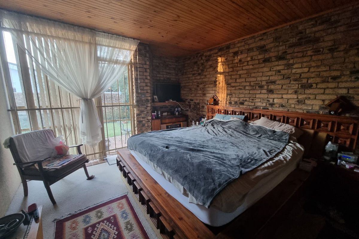 Spacious bedroom featuring exposed brick walls, a timber-paneled ceiling, and large sliding glass doors providing direct access to the rear garden area.