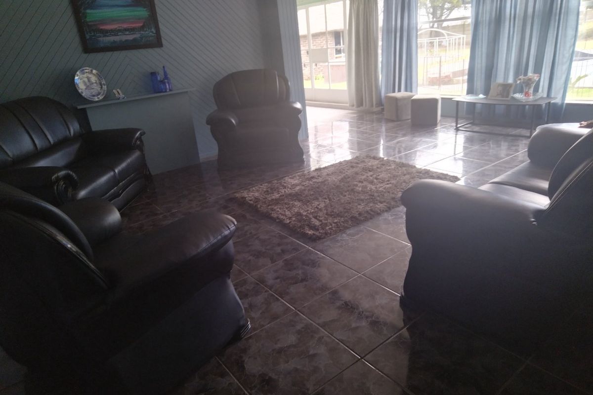 A spacious living room featuring tiled flooring, panelled walls, and large windows providing natural light and access to an outdoor patio area.