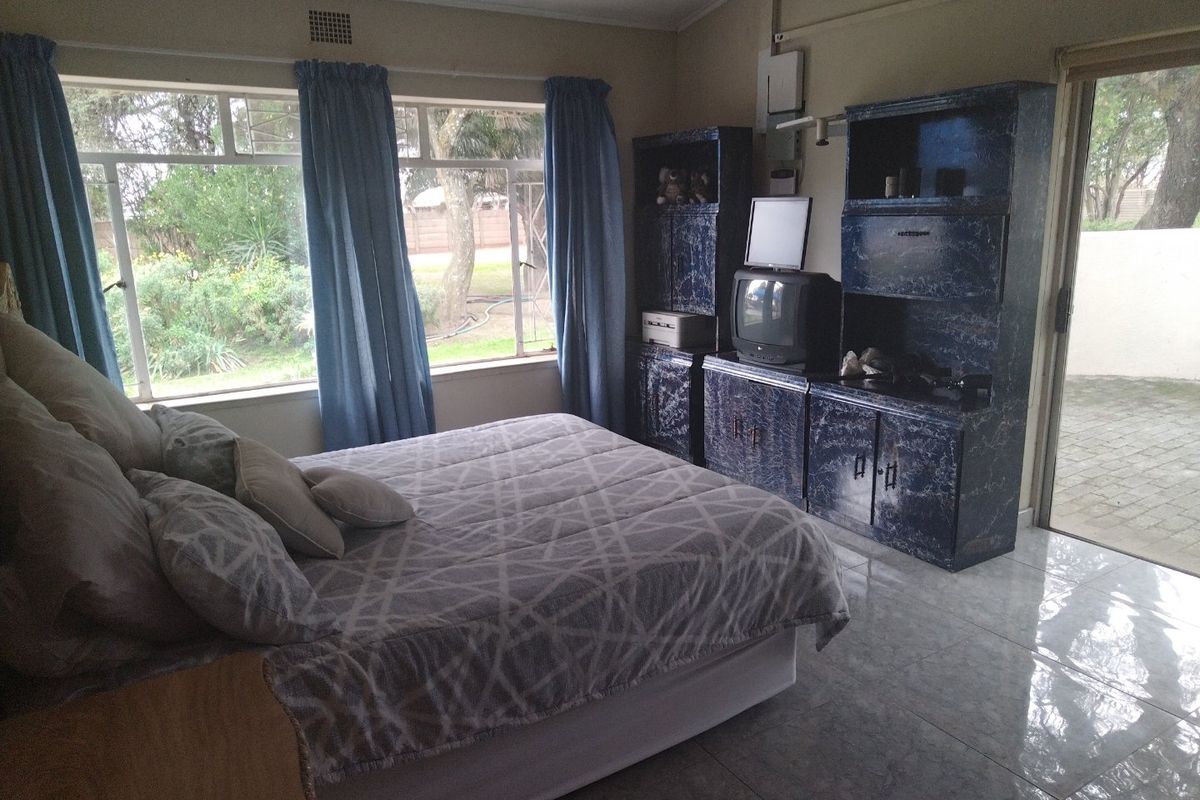 A bedroom featuring large windows with garden views, tiled flooring, and built-in storage cabinetry, with direct access to an outdoor patio area.