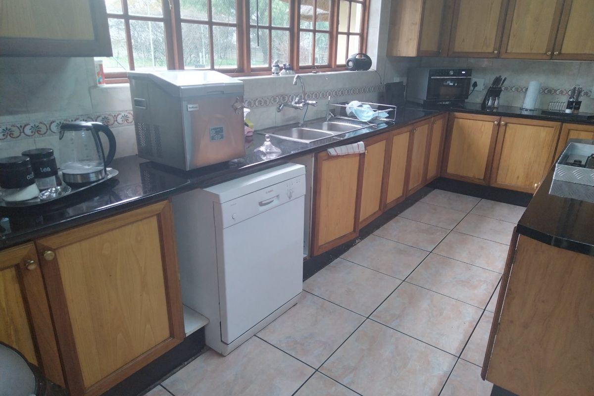 A functional kitchen featuring wooden cabinetry, dark granite countertops, double basin sink, and tiled flooring with large windows providing natural light.