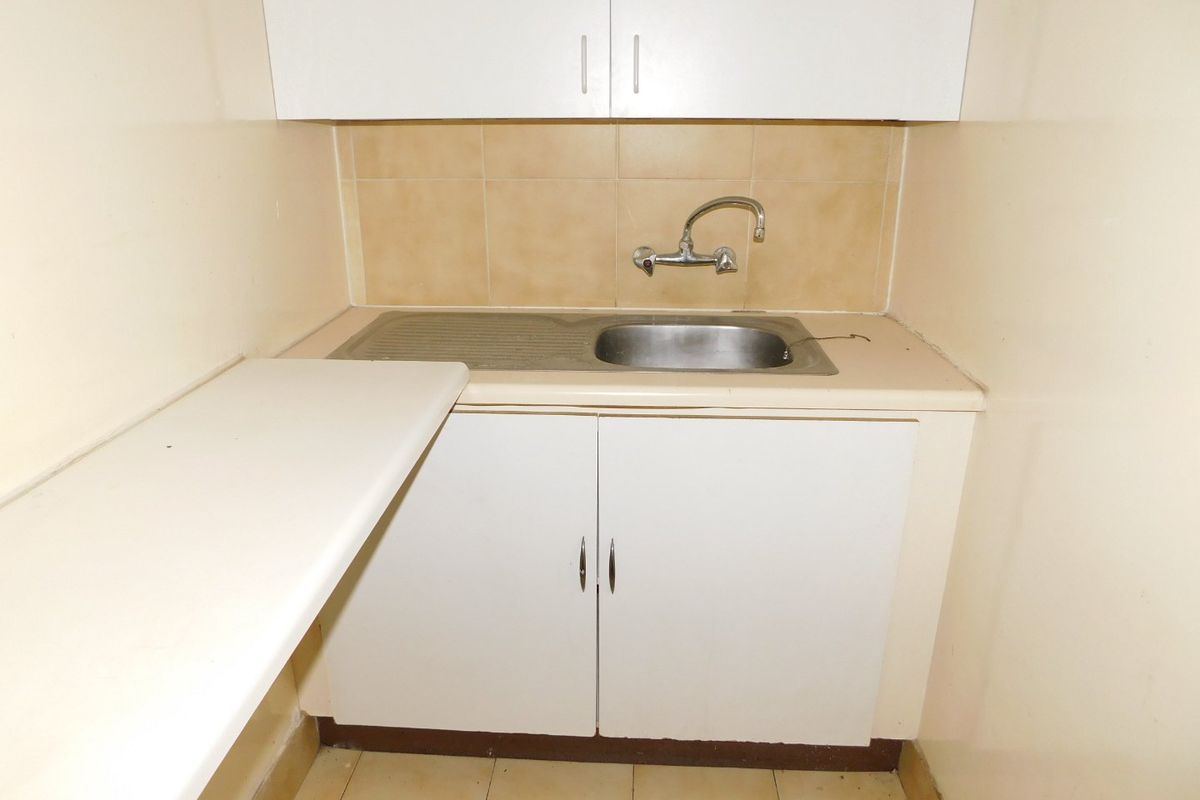 A compact kitchenette area featuring basic white cabinetry, a stainless steel sink with a mixer tap, and tiled splashback.