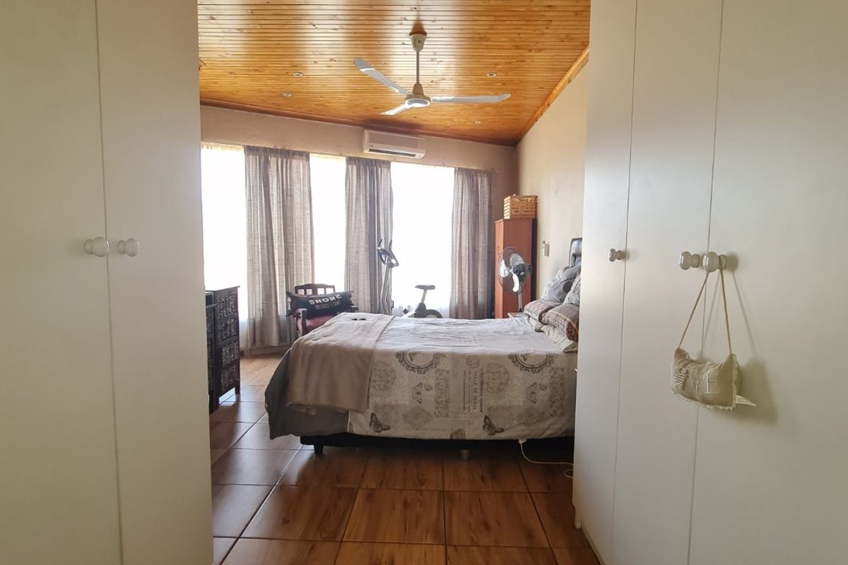 Spacious bedroom featuring a high timber-paneled ceiling, tiled flooring, and built-in floor-to-ceiling wardrobes, offering a warm and functional living space.