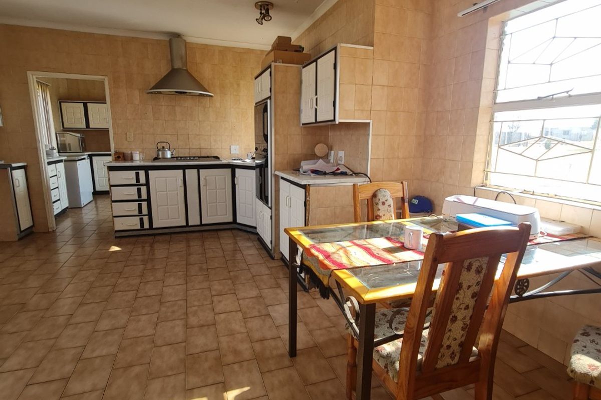 Spacious kitchen featuring tiled flooring, built-in cabinetry, stainless steel extractor fan, and an adjoining scullery area with natural light.