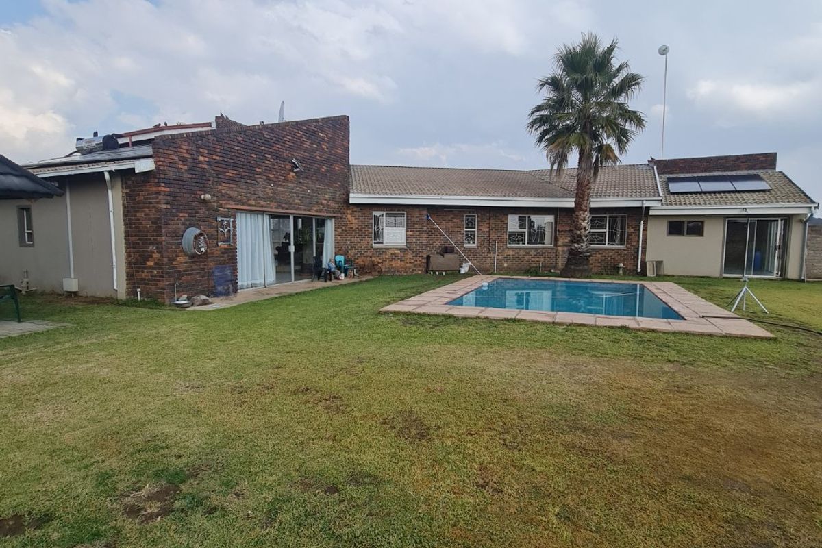 Rear view of the farm property featuring a brick facade, a swimming pool, and a spacious lawn area under a clear sky.
