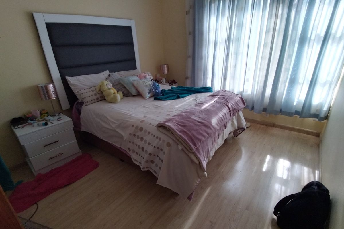 A bedroom featuring light-toned laminate flooring, a large window with sheer curtains, and a neutral wall finish.