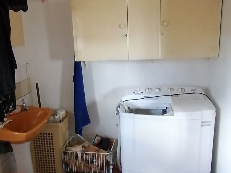 A functional laundry area featuring wall-mounted storage cabinetry and a basin, offering potential for modernization and improved utility space organization.