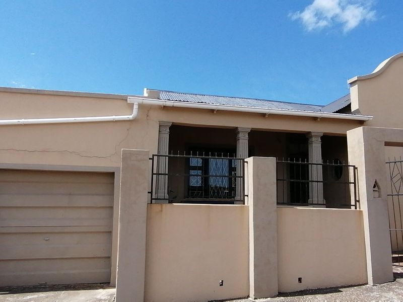 Front elevation of a house featuring a garage, perimeter wall with security gate, and decorative architectural columns.
