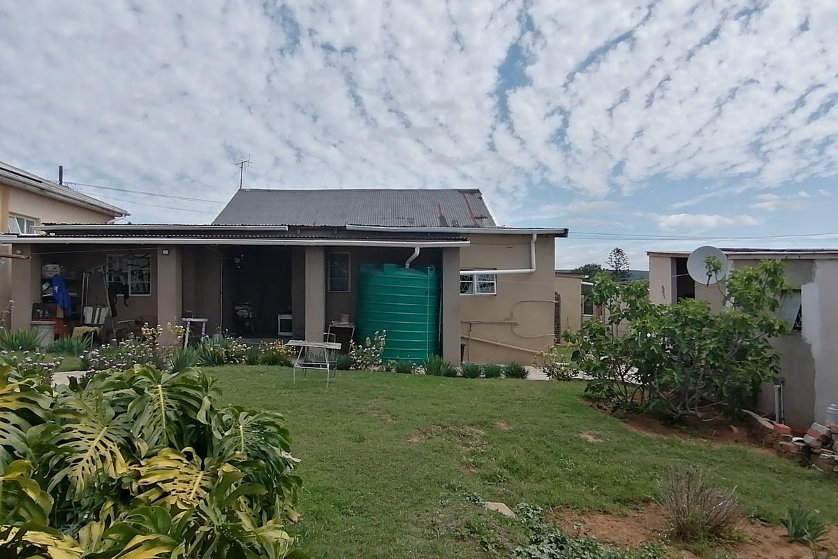 Rear view of the property featuring a garden, concrete patio area, and a large water storage tank against the main building structure.