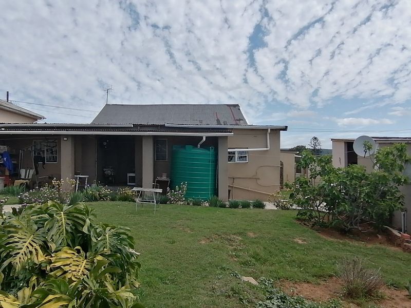 Rear view of the property featuring a garden, concrete patio area, and a large water storage tank against the main building structure.