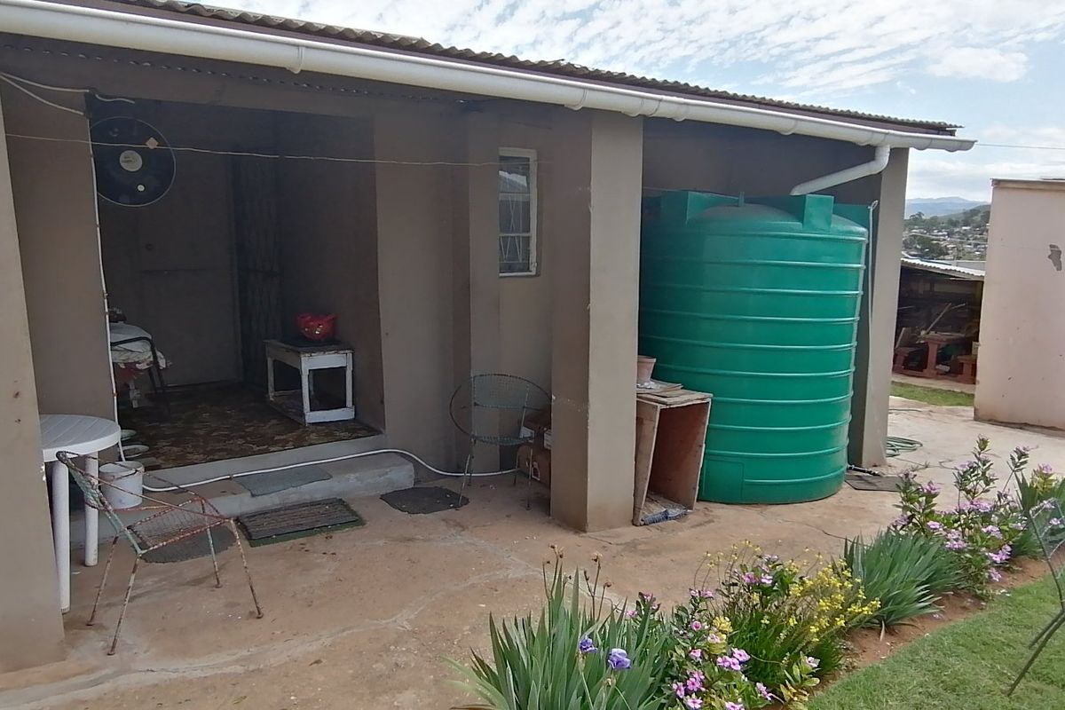 A covered patio area featuring a large water storage tank, concrete pillars, and direct access to the garden and rear yard.