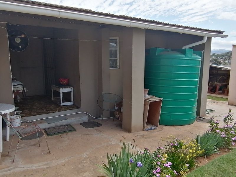 A covered patio area featuring a large water storage tank, concrete pillars, and direct access to the garden and rear yard.