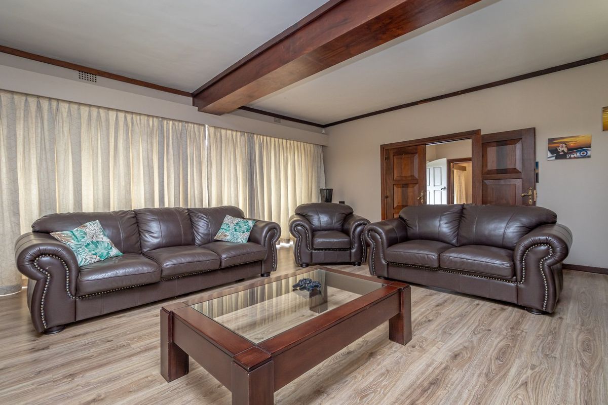 A spacious living room featuring exposed timber ceiling beams, wood-look laminate flooring, and classic wooden double doors leading to an adjacent room.