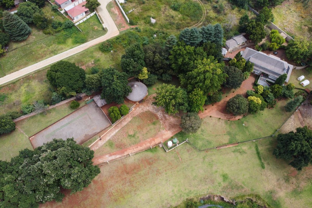 Aerial view of a large residential property featuring a main dwelling, a tennis court, mature trees, and extensive landscaped grounds.