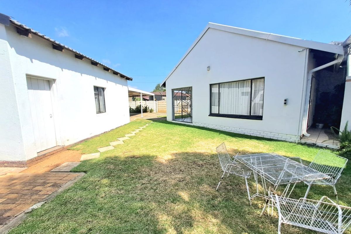 A view of the rear garden area featuring a lawn, paved pathway, and exterior building elevations with security gates and windows.
