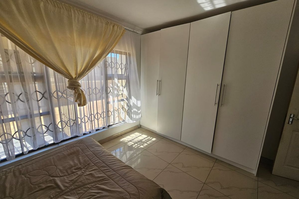 A bright bedroom featuring large built-in wardrobes, tiled flooring, and security bars on the windows.