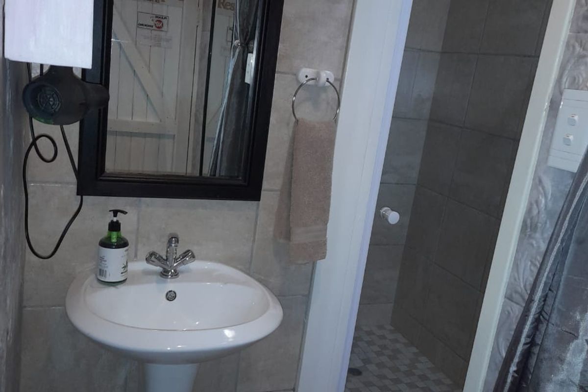 A functional bathroom featuring a pedestal basin, wall-mounted mirror, and a separate shower enclosure with tiled walls and flooring.