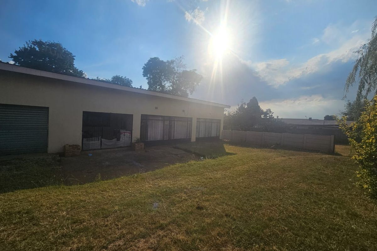 Rear view of the property featuring a large lawn, precast boundary wall, and access to the garage and main living area via sliding doors.