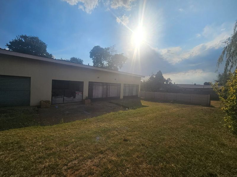 Rear view of the property featuring a large lawn, precast boundary wall, and access to the garage and main living area via sliding doors.