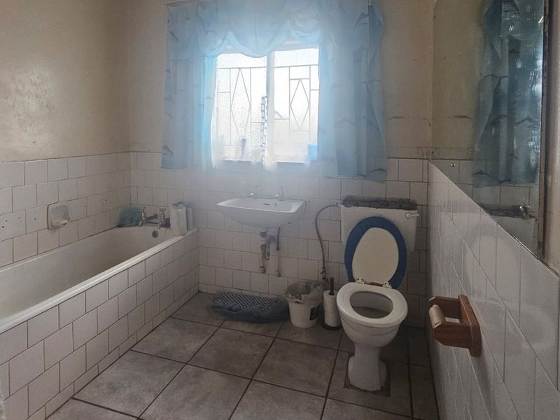 A dated bathroom featuring a standard bathtub, wall-mounted basin, and toilet with original ceramic tiling throughout, requiring modernization and cosmetic updates.