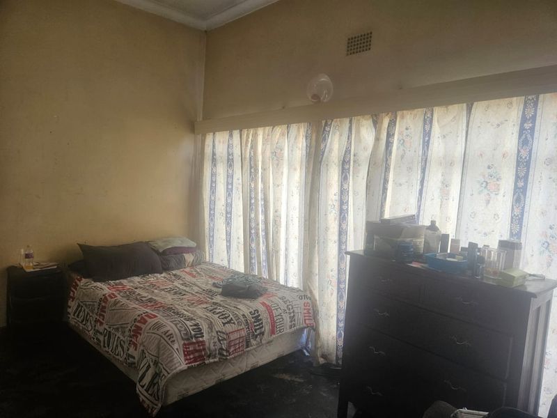 A bedroom featuring a large window with curtain rails and a ventilation grille, requiring cosmetic updates to the wall finishes.