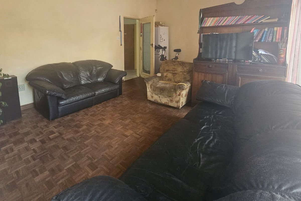 A living room featuring traditional parquet flooring and neutral wall finishes, offering a functional space with potential for cosmetic updates.