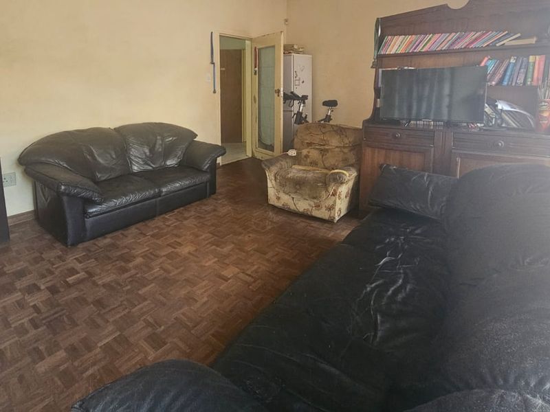 A living room featuring traditional parquet flooring and neutral wall finishes, offering a functional space with potential for cosmetic updates.