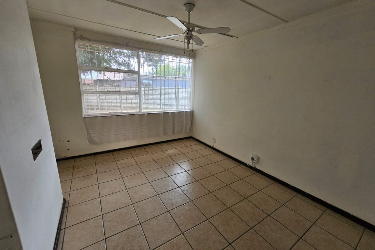 A vacant bedroom featuring tiled flooring, a ceiling fan, and security bars on the window.