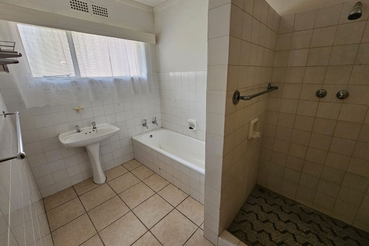 A functional bathroom featuring a pedestal basin, a built-in bathtub, and a separate walk-in shower with tiled finishes.
