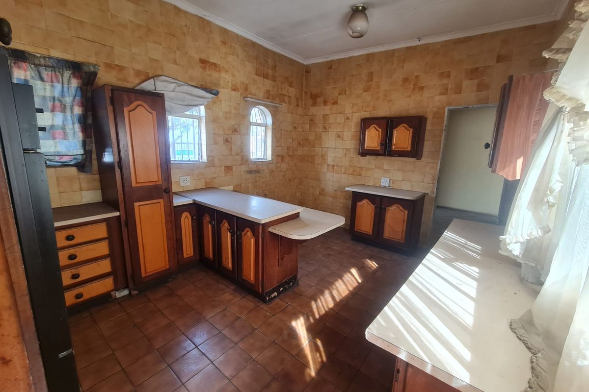 A dated kitchen featuring traditional wooden cabinetry, tiled walls, and tiled flooring, offering a functional layout with ample counter space.