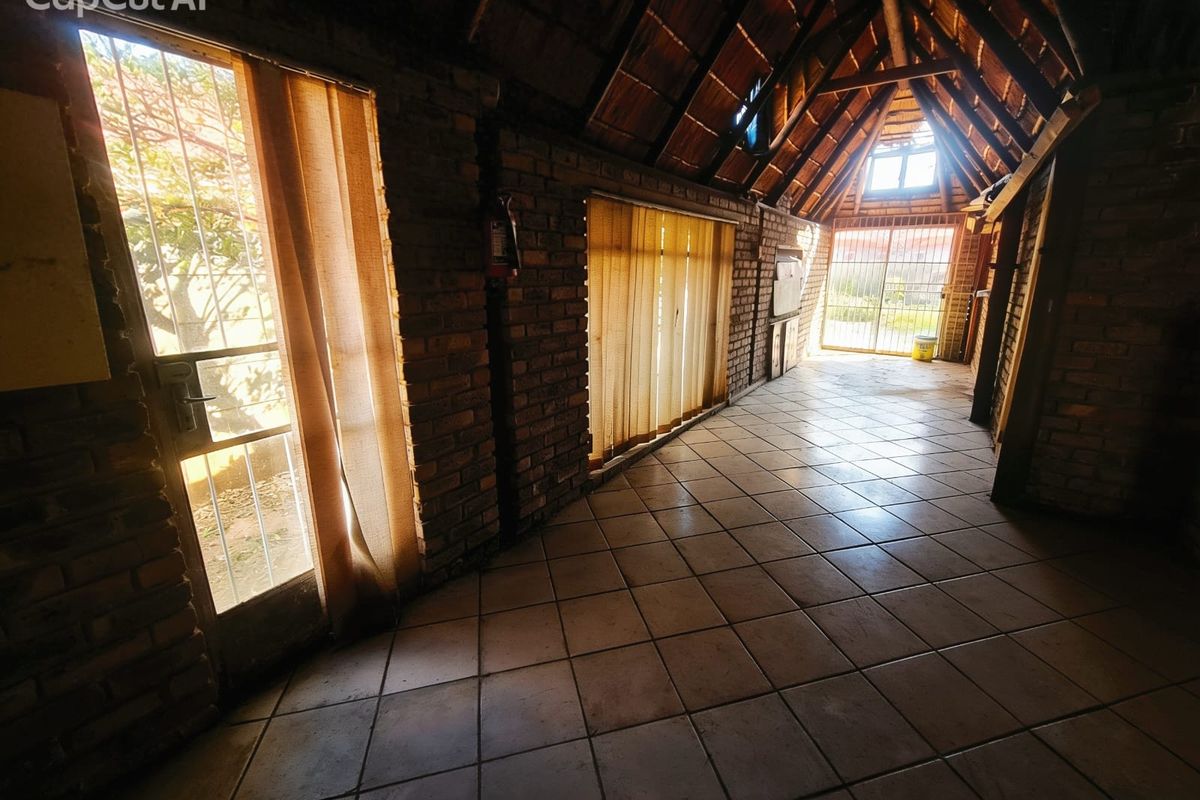Spacious interior area featuring exposed brick walls, vaulted timber-beamed ceiling, and tiled flooring with multiple access points to the exterior.