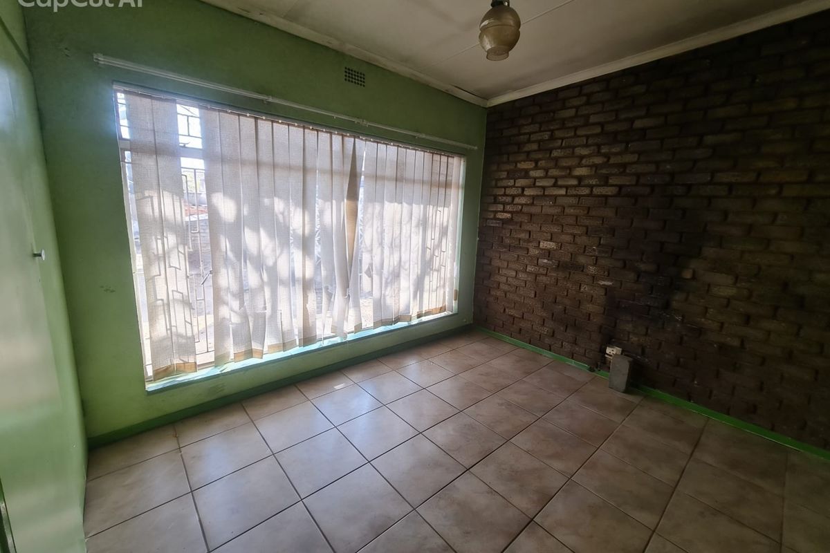 An empty bedroom featuring a prominent exposed brick feature wall, tiled flooring, and a large window with vertical blinds.