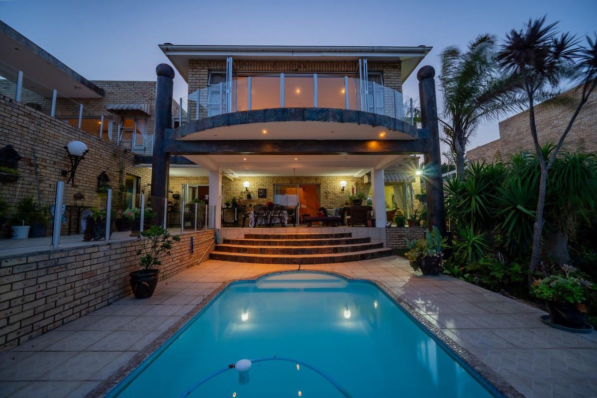 Rear exterior view of a two-story brick house featuring a swimming pool, tiled patio area, and an upper-level balcony with glass balustrades.