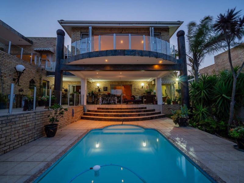 Rear exterior view of a two-story brick house featuring a swimming pool, tiled patio area, and an upper-level balcony with glass balustrades.