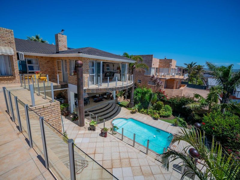 Spacious rear exterior featuring a tiled patio, swimming pool, glass balustrades, and brick facade, offering an ideal outdoor entertainment area.