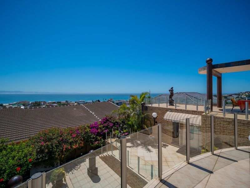 Spacious multi-level outdoor terrace featuring glass balustrades, tiled flooring, and a pergola, offering expansive elevated coastal and neighbourhood views.