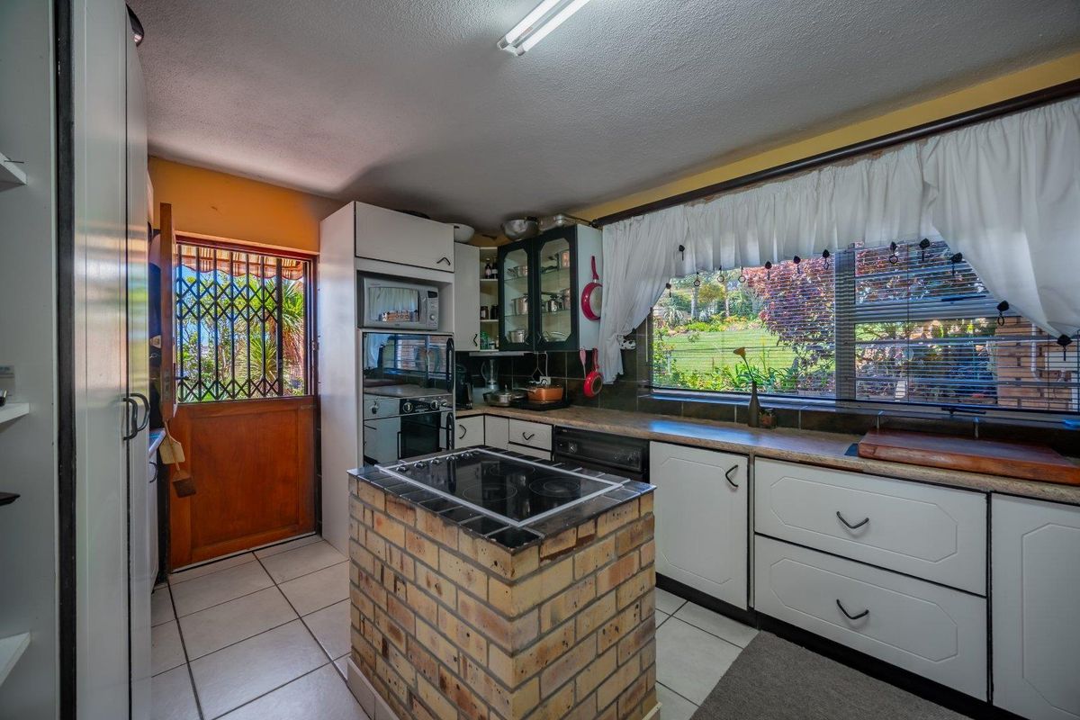 A functional kitchen featuring a unique brick island, built-in appliances, tiled flooring, and direct access to the garden through a security-gated door.