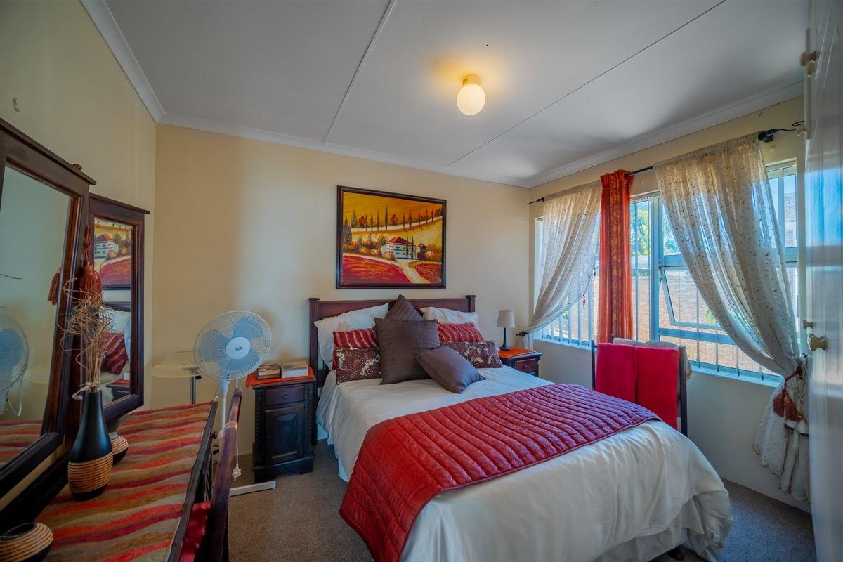 A cozy bedroom featuring neutral walls, carpeted flooring, and a window fitted with security bars, providing a functional and comfortable living space.