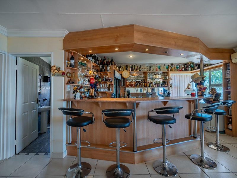 A dedicated home bar area featuring a custom timber counter, mirrored shelving, recessed lighting, and tiled flooring, providing a functional space for entertaining.