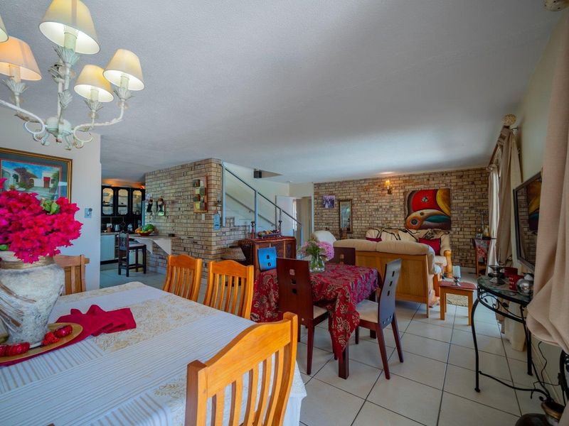 Spacious open-plan living and dining area featuring exposed brick walls, ceramic tile flooring, and an integrated kitchen space with a staircase.