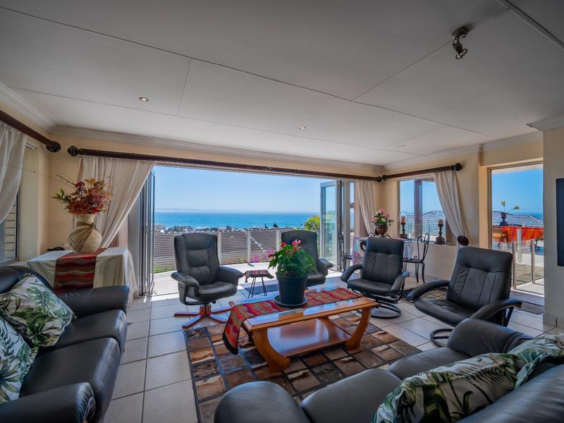 Spacious living room featuring large bi-fold doors that open to a balcony with expansive ocean views, tiled flooring, and recessed lighting.