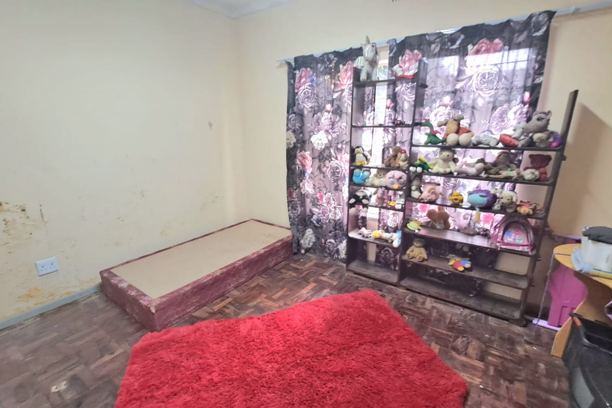 A bedroom featuring parquet flooring and a window with curtains. The walls show significant signs of surface damage and wear.