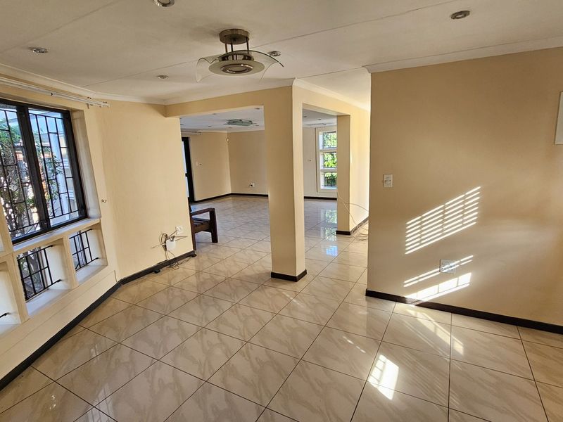 Spacious open-plan living area featuring neutral tiled flooring, recessed ceiling lighting, and large windows with security bars, offering a bright and versatile layout.