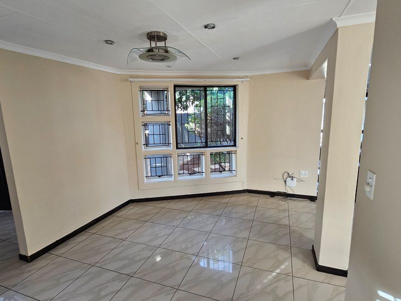 A bright, open-plan living area featuring neutral tiled flooring, recessed ceiling lighting, and security bars on the windows.